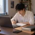 Student completing online coursework at home alongside his school notebooks.